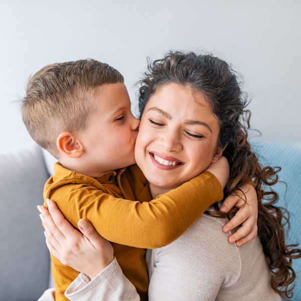 woman hugging young son while receiving a kiss on the cheek